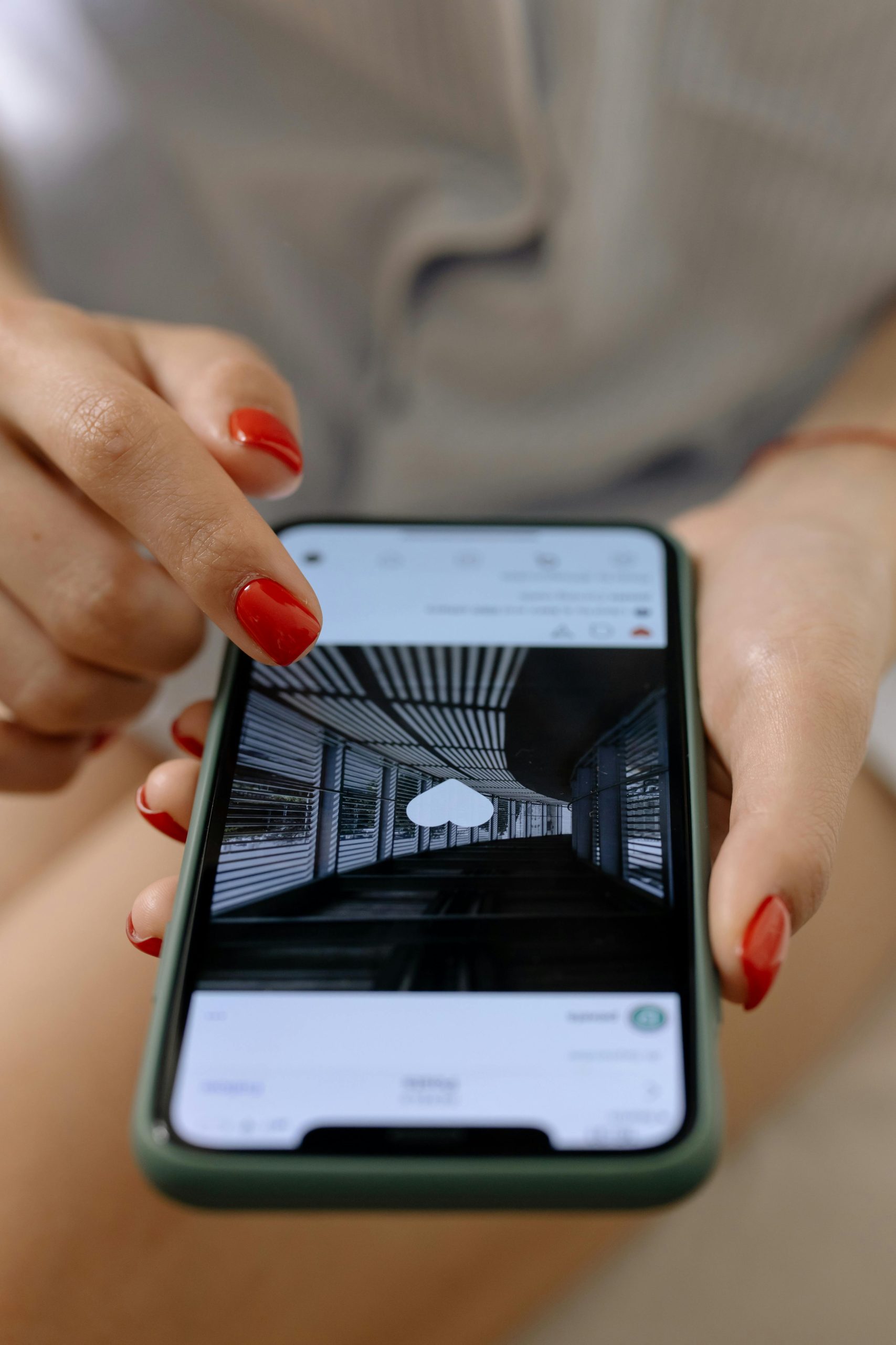 Engagement: A woman with red nails uses a smartphone to browse social media indoors.